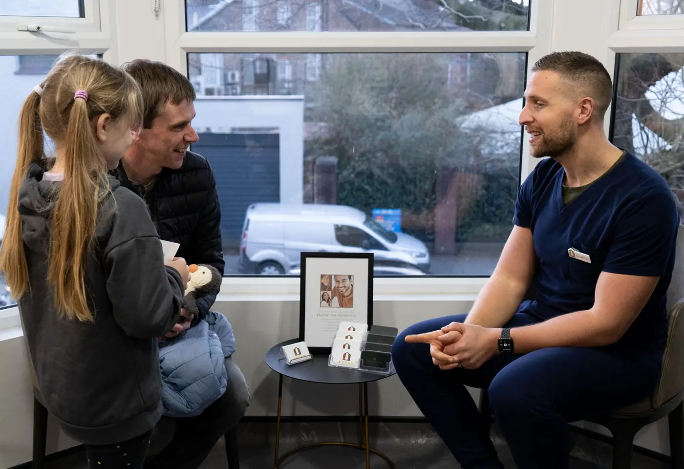 A dentist talking with a father and daughter in the waiting area